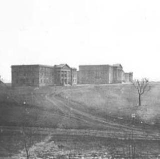 Three brick buildings, each several stories high, stand isolated on a treeless prairie